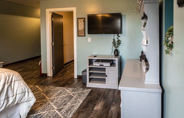 A bedroom with a bed, a TV, a small shelf, and a door leading to another room. - "The Barn at Sunset Lane" - Spacious 4BR Home on 16 Acres (Killbuck)