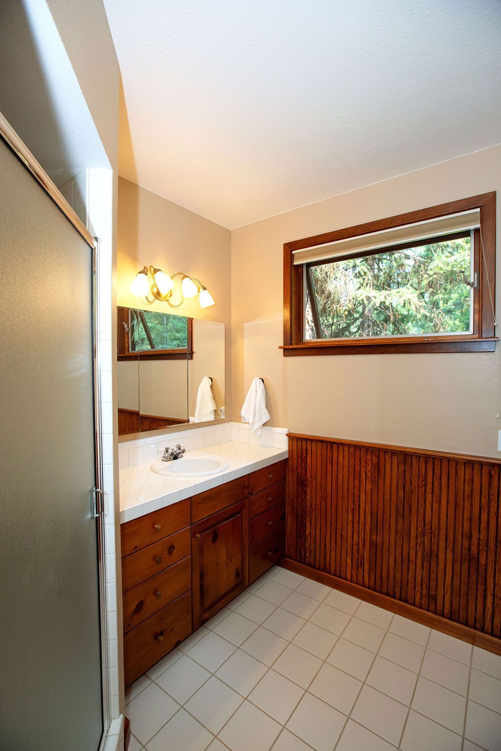 A bathroom with a wooden vanity, a white sink, and a mirror with lights.