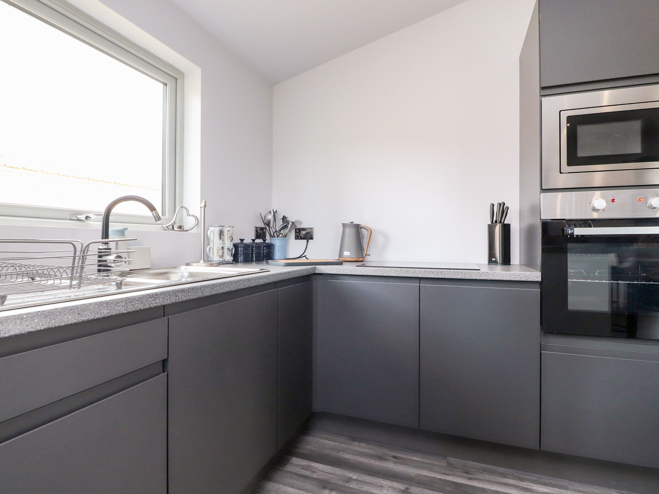 A modern kitchen with grey cabinets, a stainless steel oven, and a window above the sink.