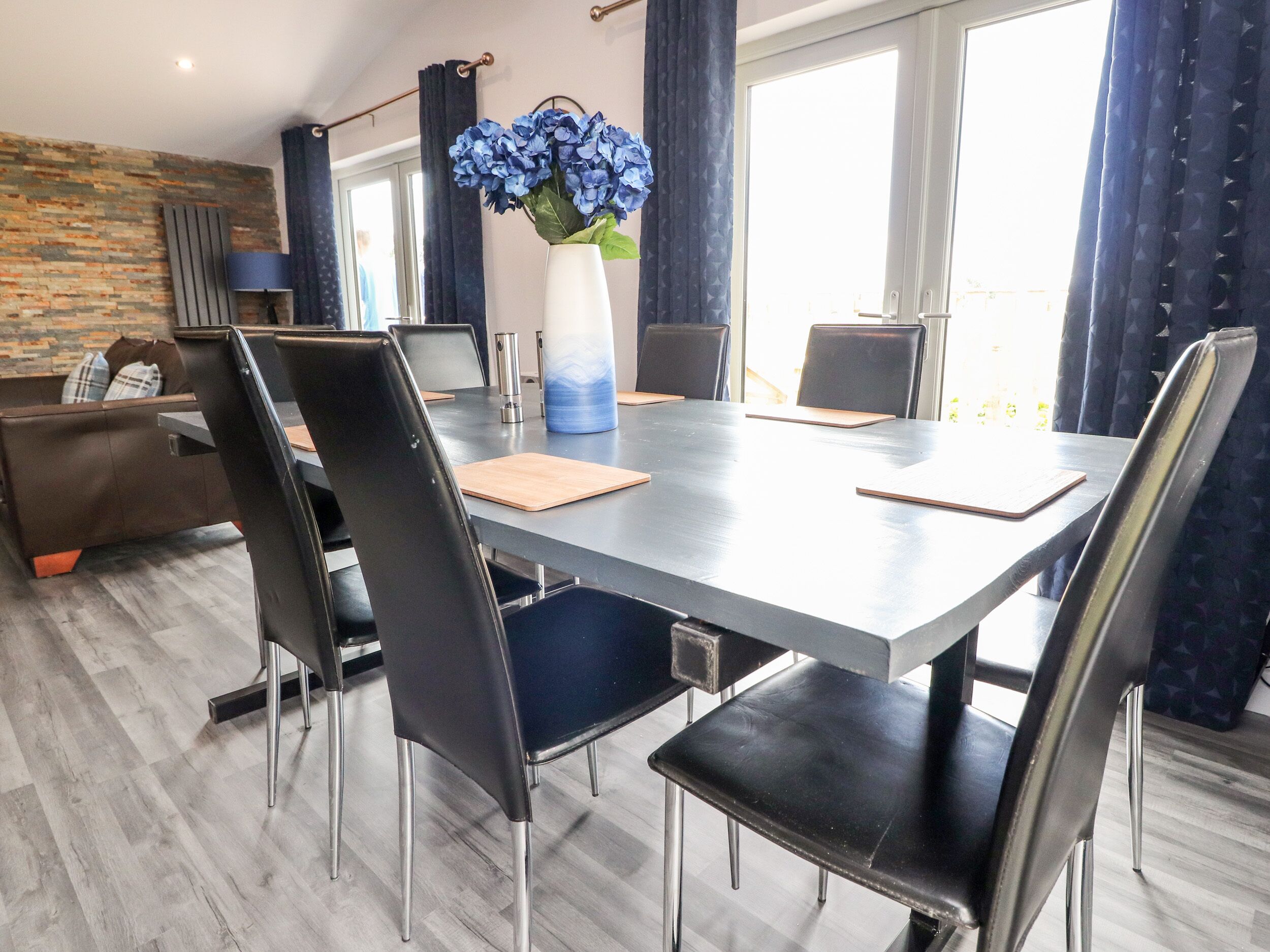 Un comedor moderno con una mesa larga, sillas negras y un jarrón de flores azules.