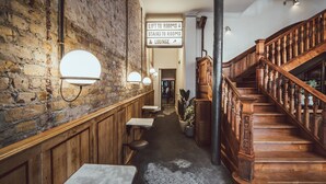 A narrow hallway with a brick wall, wooden benches, and a staircase. - The Pilgrm Hotel (London)