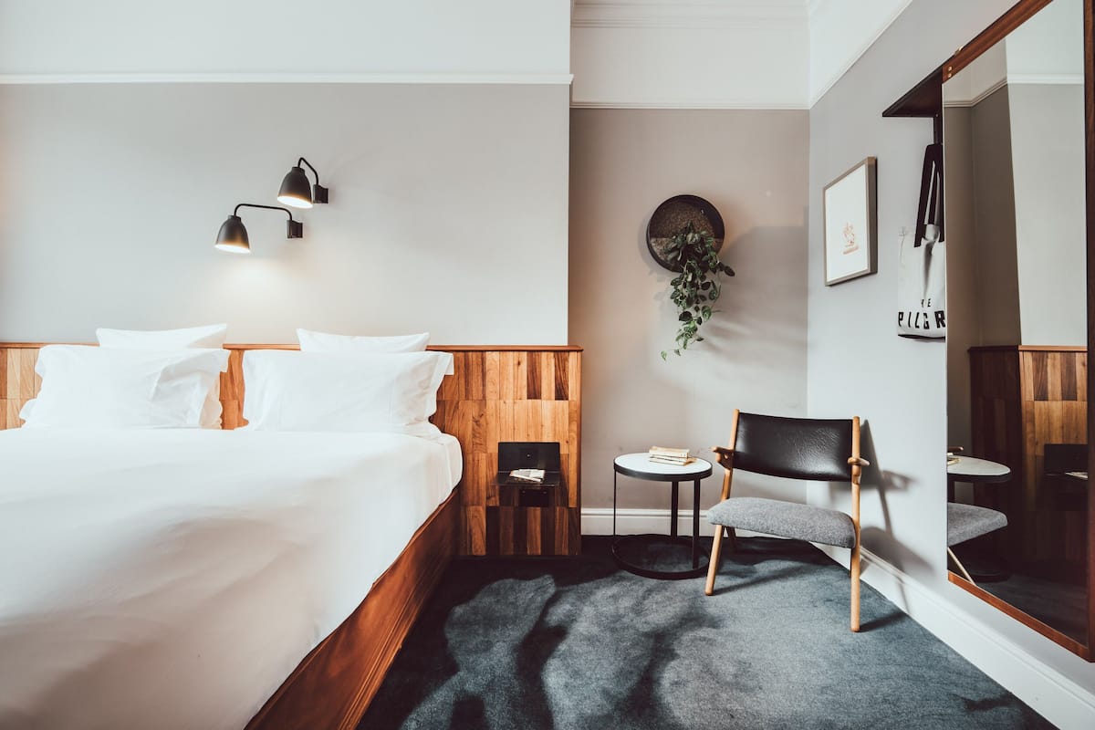 Una habitación de hotel moderna con una cama grande, una mesita redonda pequeña, una silla y un espejo.
