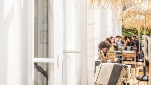 An open door leading to an outdoor seating area with tables and chairs, a straw umbrella, and a view of a building in the background. - The Pilgrm Hotel (London)