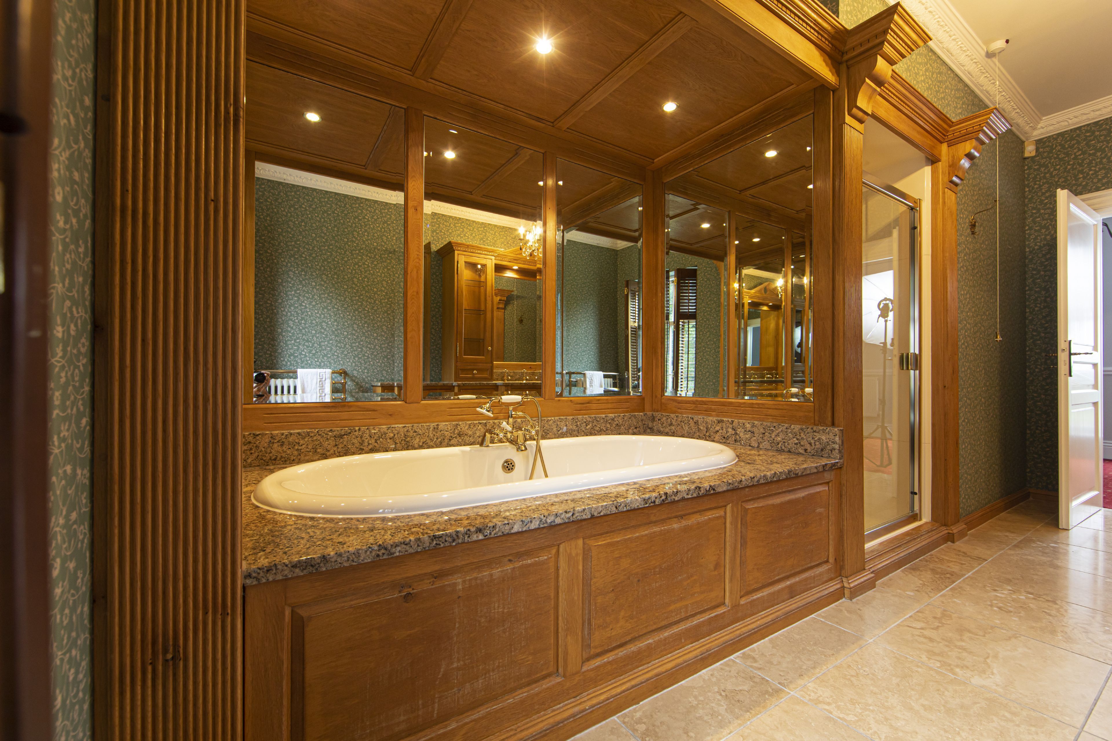 A large, freestanding bathtub with a granite countertop, wooden paneling, and a large mirror above it.