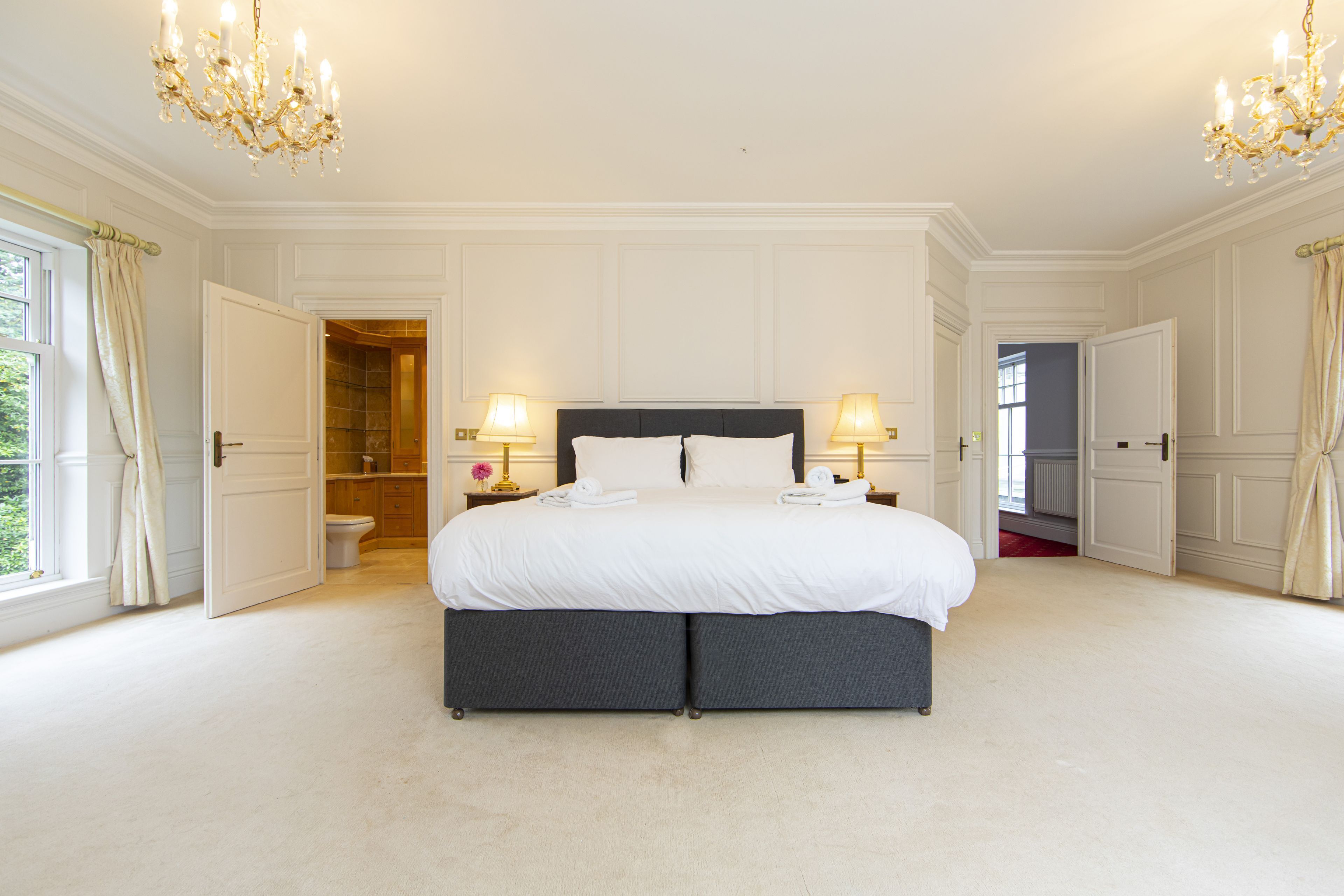 A spacious bedroom with a large bed, two bedside lamps, and a chandelier.