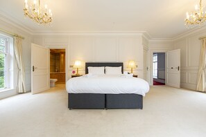 A spacious bedroom with a large bed, two bedside lamps, and a chandelier. - NEW Listing -  Fairytale Manor House with Indoor Swimming Pool (Swansea)