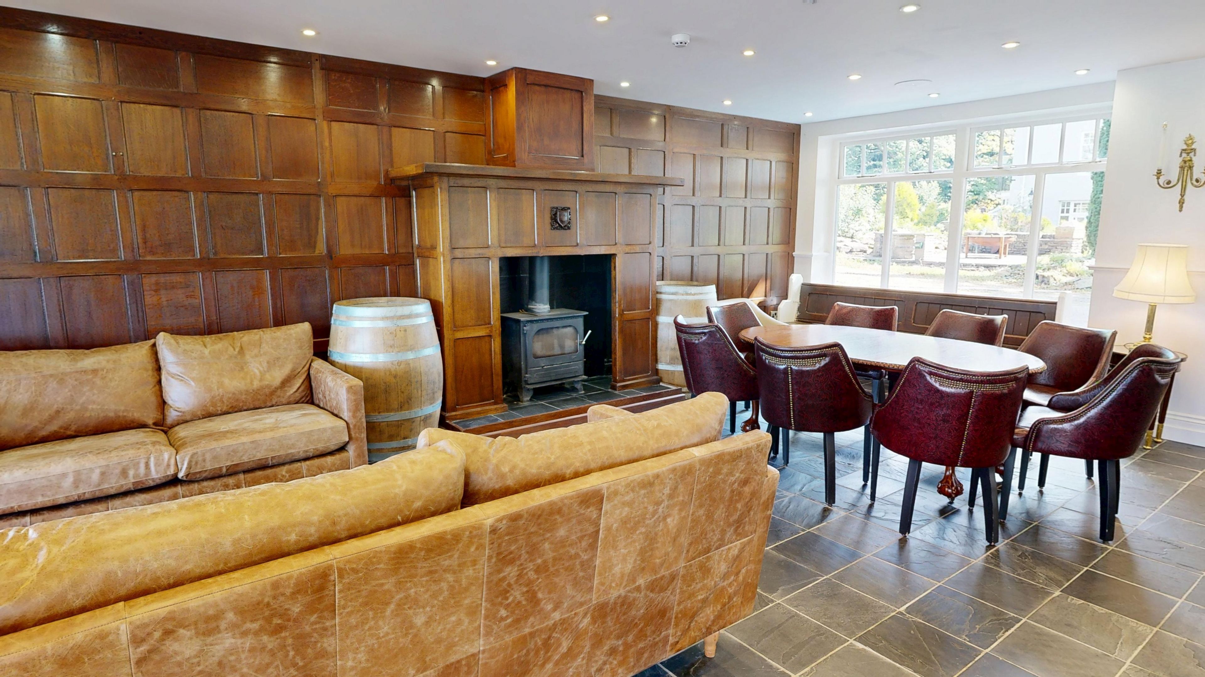 A cozy living room with a fireplace, wooden paneling, a sofa, and a dining area with chairs.