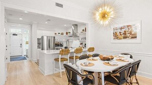 A modern kitchen with white cabinetry, a stainless steel refrigerator, and a dining area with a round table and wicker chairs.