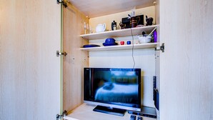 A compact entertainment unit with a flat-screen TV, a remote control, and a small shelf with various items. - Entire 1bed Studio With Ensuite, Balcony & Parking (Westcliff-on-Sea)