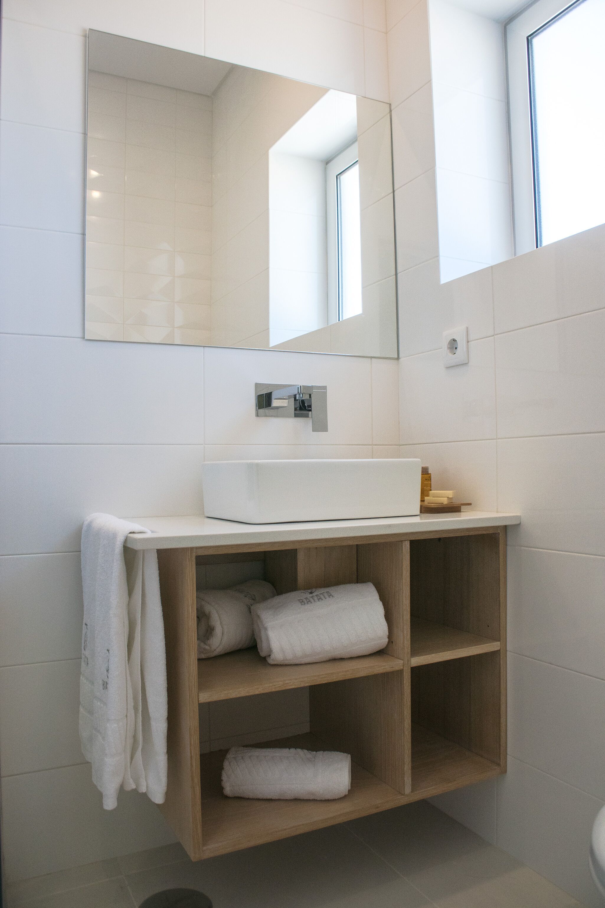 A modern bathroom with a white sink, wooden shelves, and a large mirror.