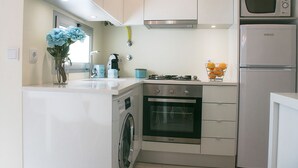 A compact kitchen with a washing machine, oven, microwave, and a gas stove. - Alojamento Batata - Peixe Imperador  (Nazaré)