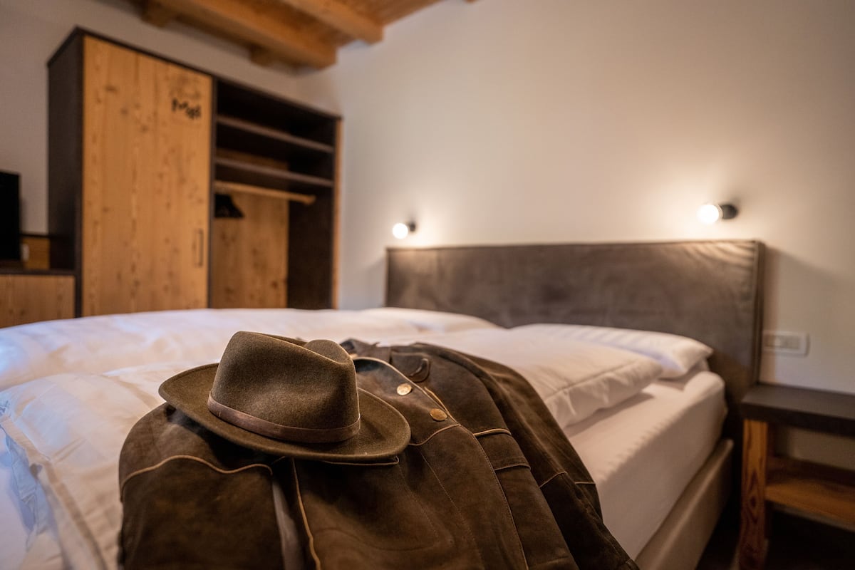 A bed with a brown hat and a brown jacket on it, wooden wardrobe, and a headboard with wall-mounted lights.