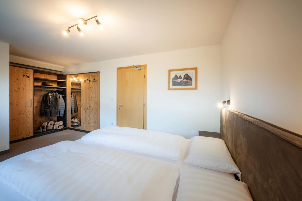 A bedroom with two beds, a wooden wardrobe, a coat rack, and a framed picture on the wall.