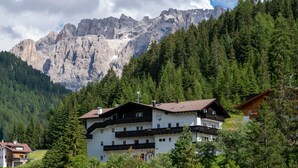 Un edificio de varios pisos con balcones, rodeado de un bosque frondoso y montañas al fondo.