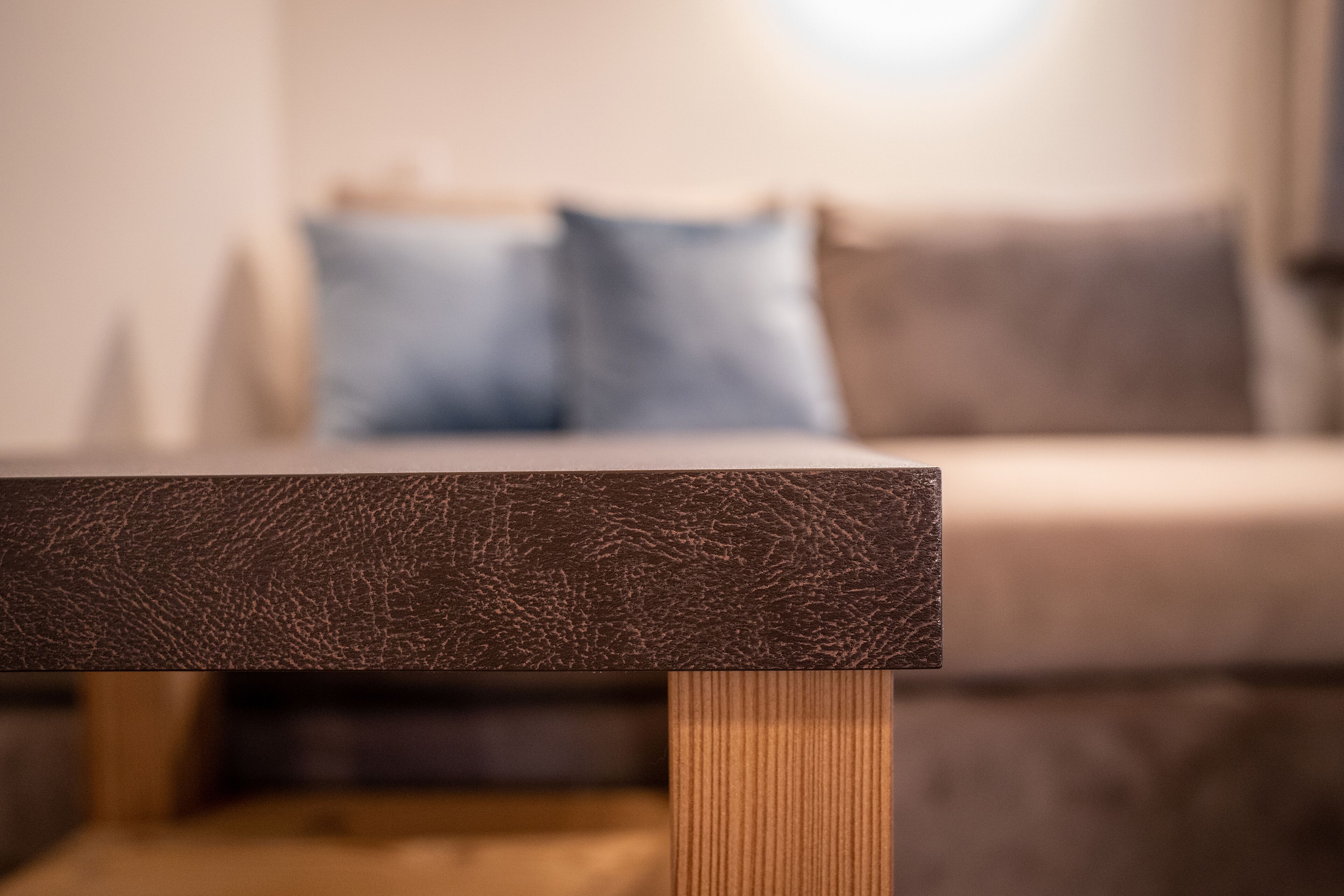 Ein Detailaufnahme eines rustikalen Holztisches, im Hintergrund verschwommen ein Bett und Kissen.