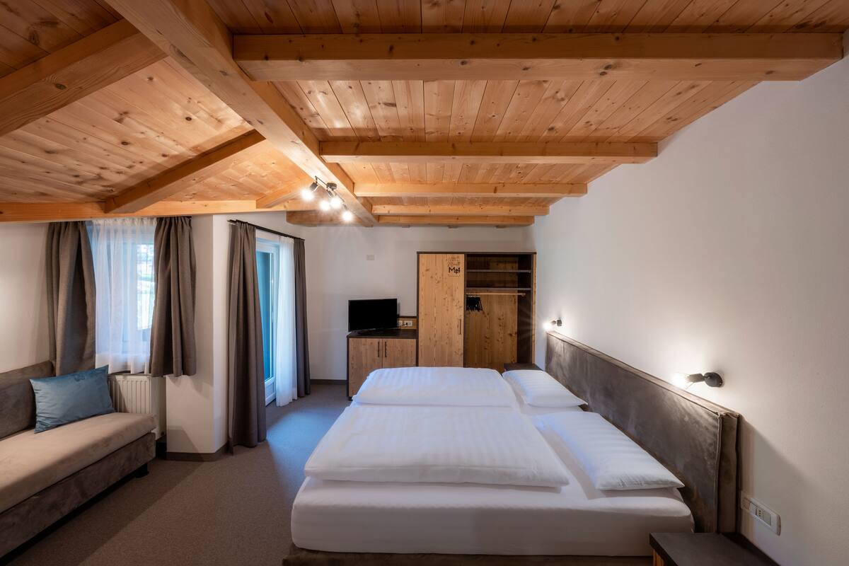 A bedroom with a wooden ceiling, a sofa, a bed, a TV, and a wardrobe.