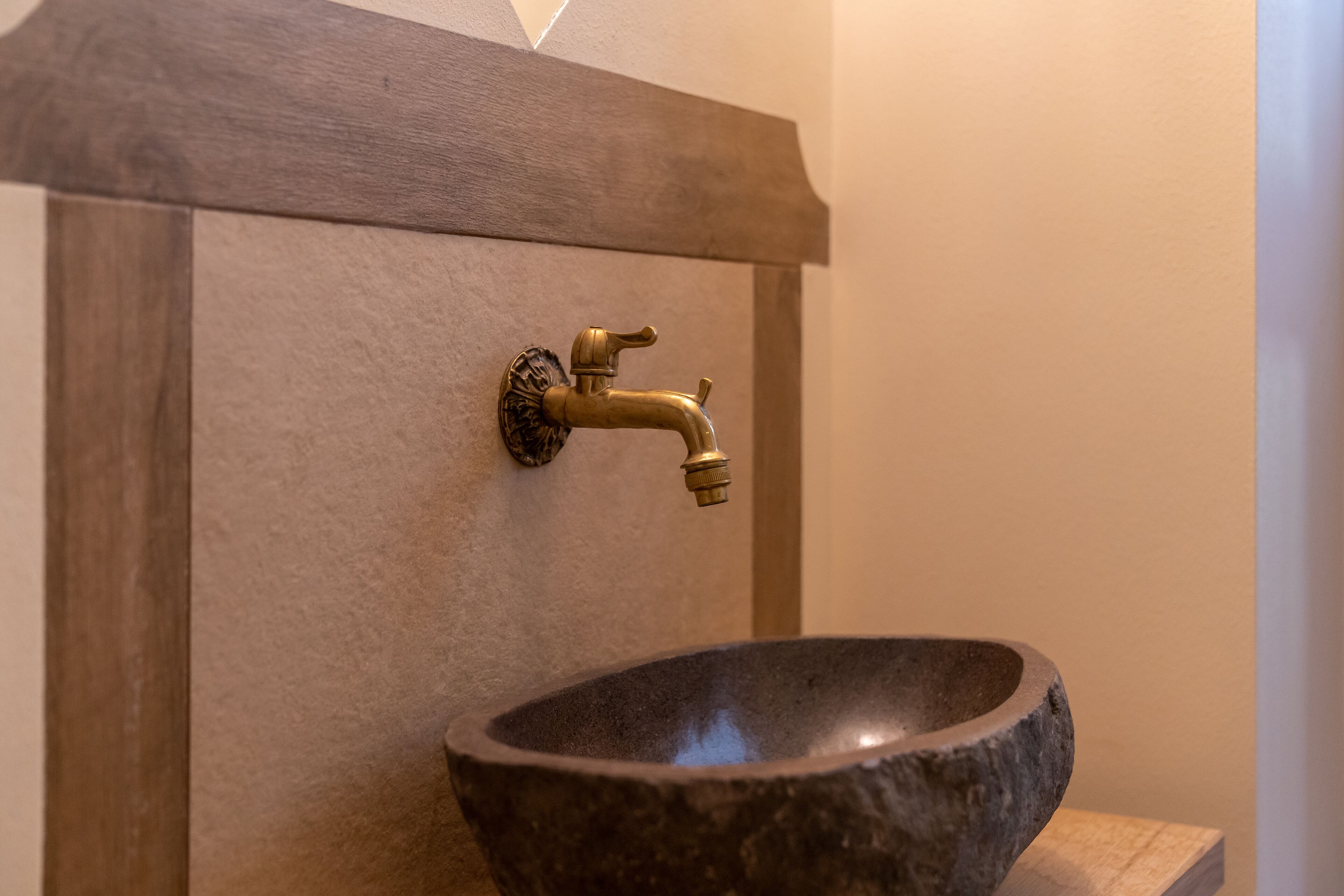 A bathroom with a stone sink and a brass faucet mounted on a wooden panel.