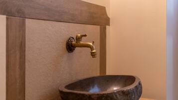 A bathroom with a stone sink and a brass faucet mounted on a wooden panel.