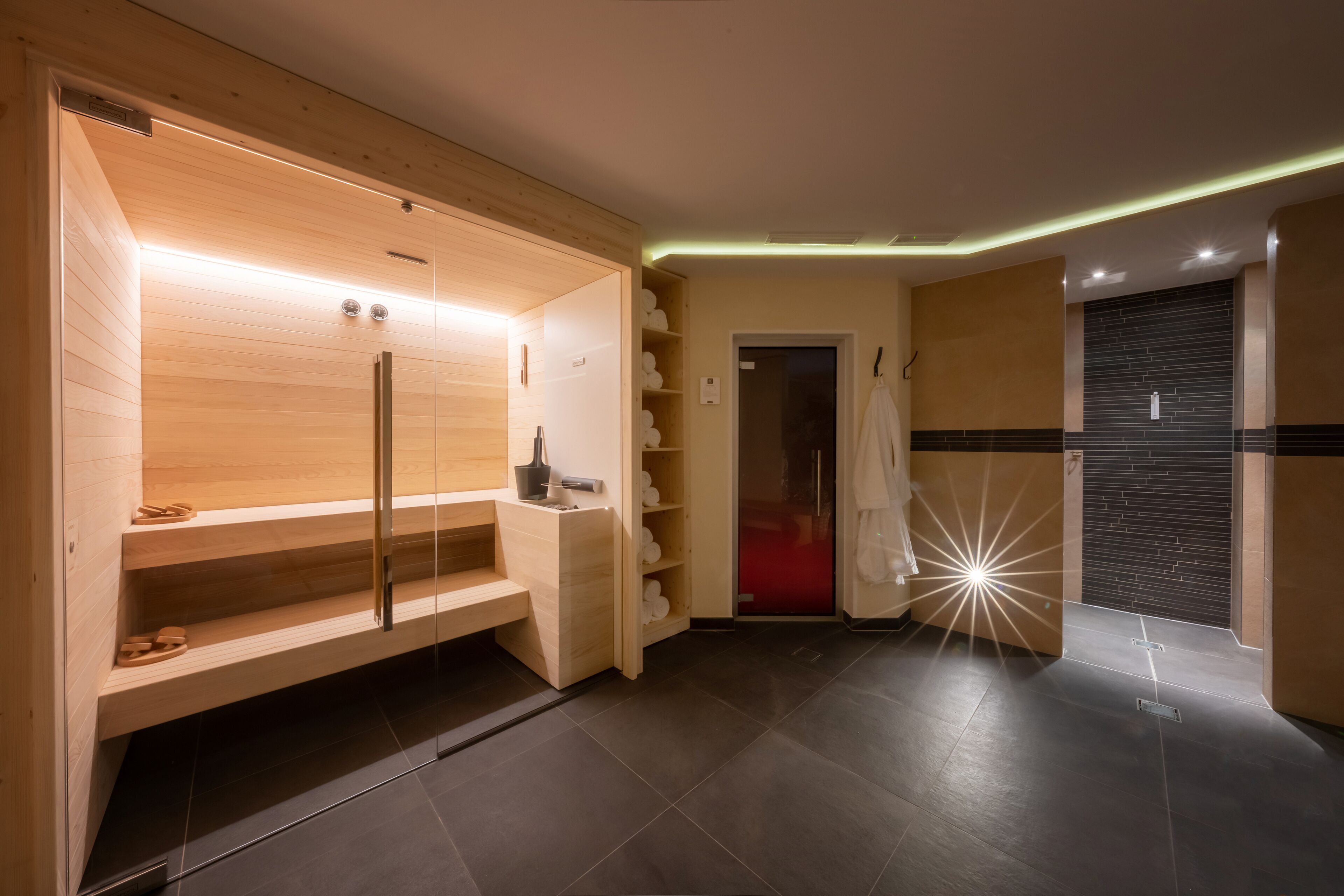 A modern spa room with a wooden sauna, a glass shower enclosure, and a red-tiled floor.