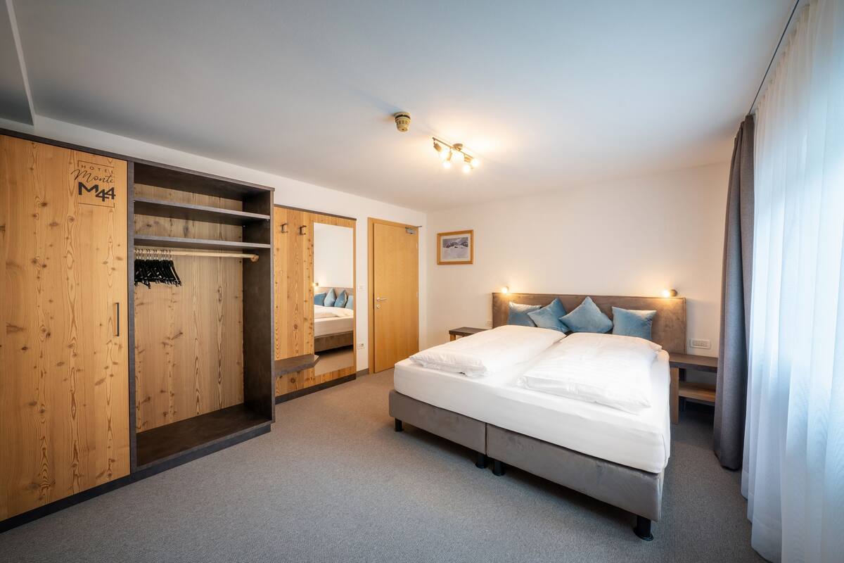 A hotel room with a large bed, wooden wardrobe, and a mirror.