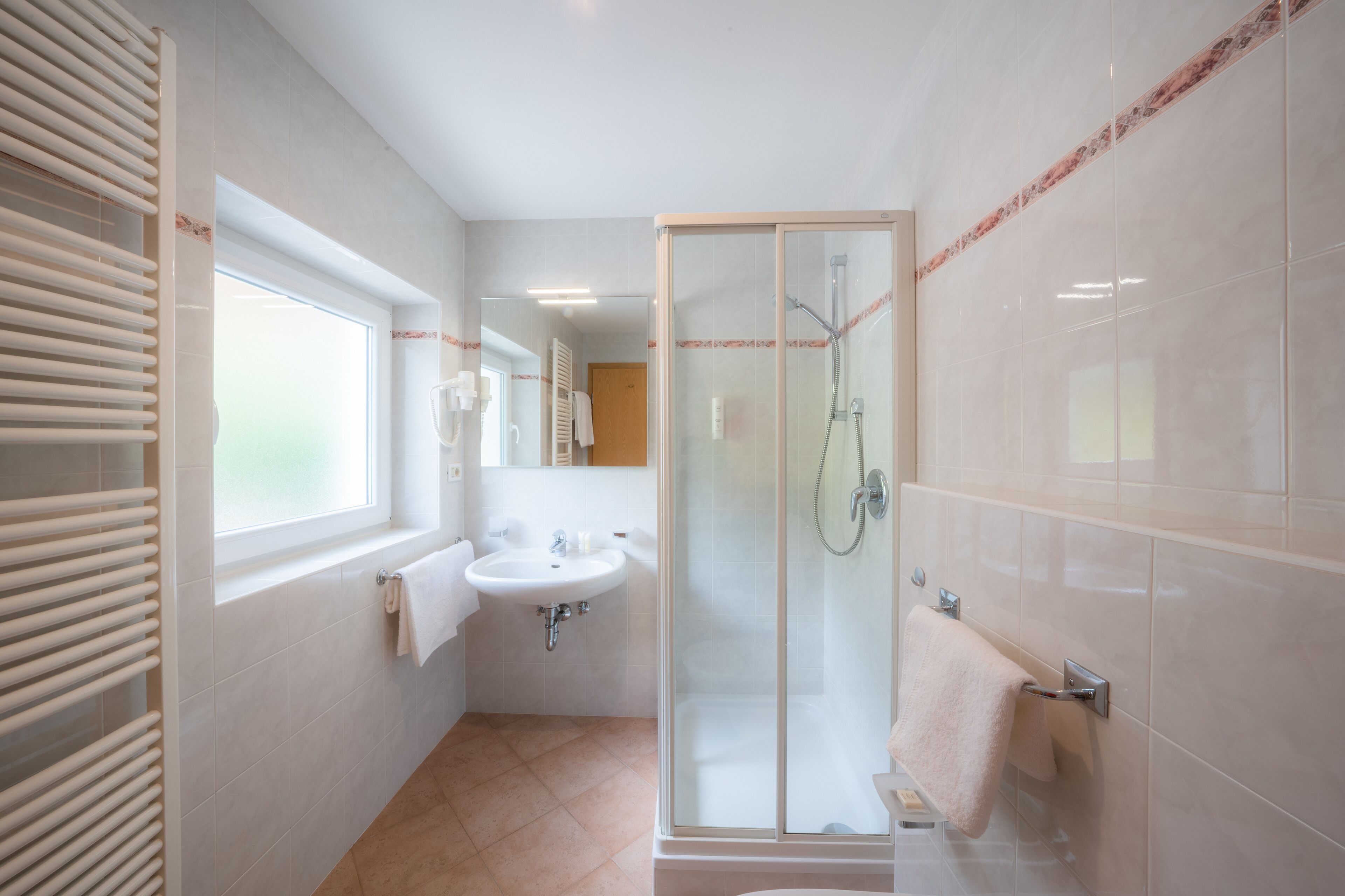 Un baño moderno con ducha envuelta en vidrio, un lavamanos y una ventana.