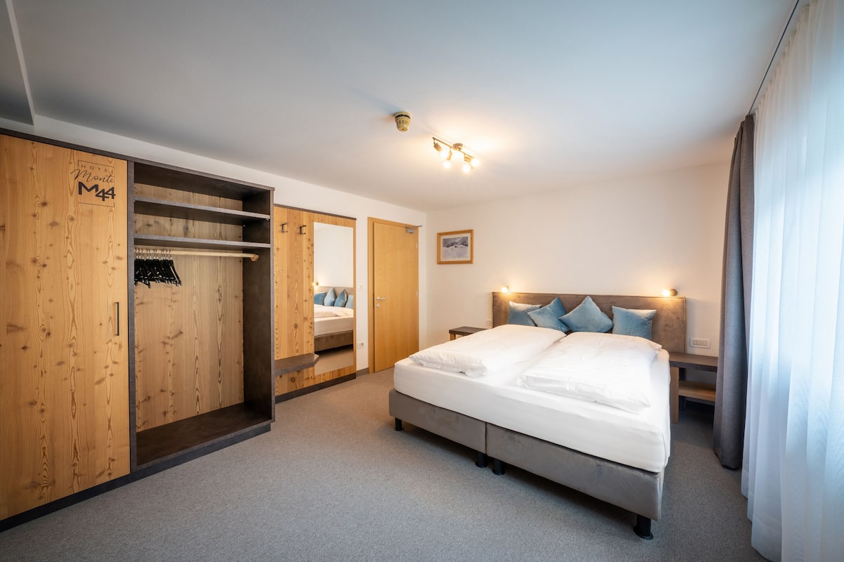 A hotel room with a large bed, wooden wardrobe, and a mirror.