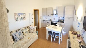 Ett kompakt bostadsutrymme med en soffa, ett matbord, stolar, ett köksutrymme och en liten tv.