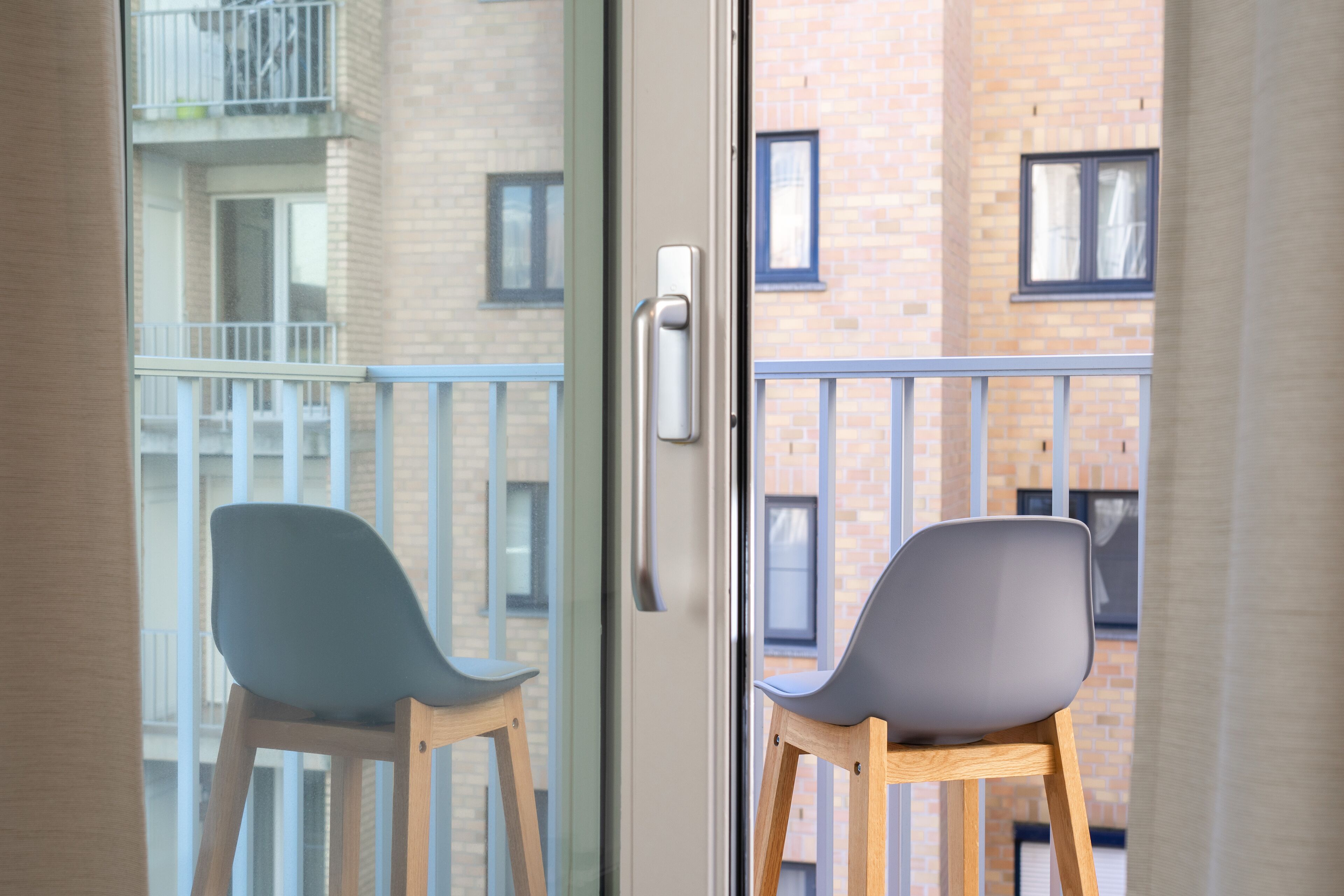 Vista desde el interior de una habitación a un balcón con dos sillas y una puerta.