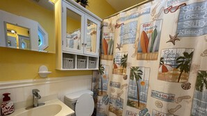 A bathroom with a toilet, sink, and a shower curtain with beach-themed designs. - Come and Relax at Paradise Found! (HATTERAS)