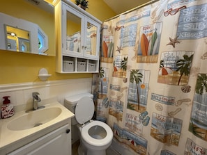 A bathroom with a toilet, sink, and a shower curtain with beach-themed designs.