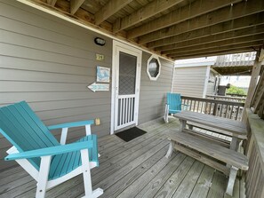 A wooden deck with two turquoise Adirondack chairs and a bench, a door with a window, and a welcome sign.