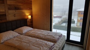 Un letto matrimoniale con biancheria bianca in una stanza con pareti in legno e un'ampia finestra.