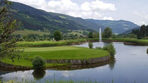Un campo da golf tranquillo con uno stagno, una fontana e colline dolci sullo sfondo.