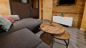 Un accogliente soggiorno con un divano grigio, un piccolo tavolino rotondo in legno e un mobiletto bianco con un televisore montato a parete.