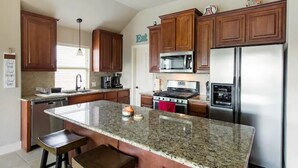 A kitchen with granite countertops, wooden cabinets, stainless steel appliances, and a central island with stools.