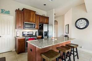 A kitchen with wooden cabinets, a granite countertop, a stainless steel refrigerator, and a clock on the wall. - Beautiful 5BD/3BA Near BLD/Waterpark/AT&T Stadium (Mansfield)