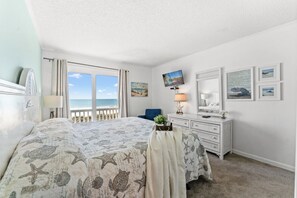 A bedroom with a large bed, a dresser, a television, and a view of the ocean. - Dunescape 201-3BR/2.5BA Oceanfront condo in Crescent Beach (North Myrtle Beach)