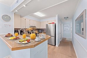 A modern kitchen with a central island, stainless steel appliances, and a breakfast setup. - Dunescape 201-3BR/2.5BA Oceanfront condo in Crescent Beach (North Myrtle Beach)
