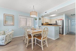 A dining area with a wooden table and chairs, a hanging light fixture, and a window with blinds.