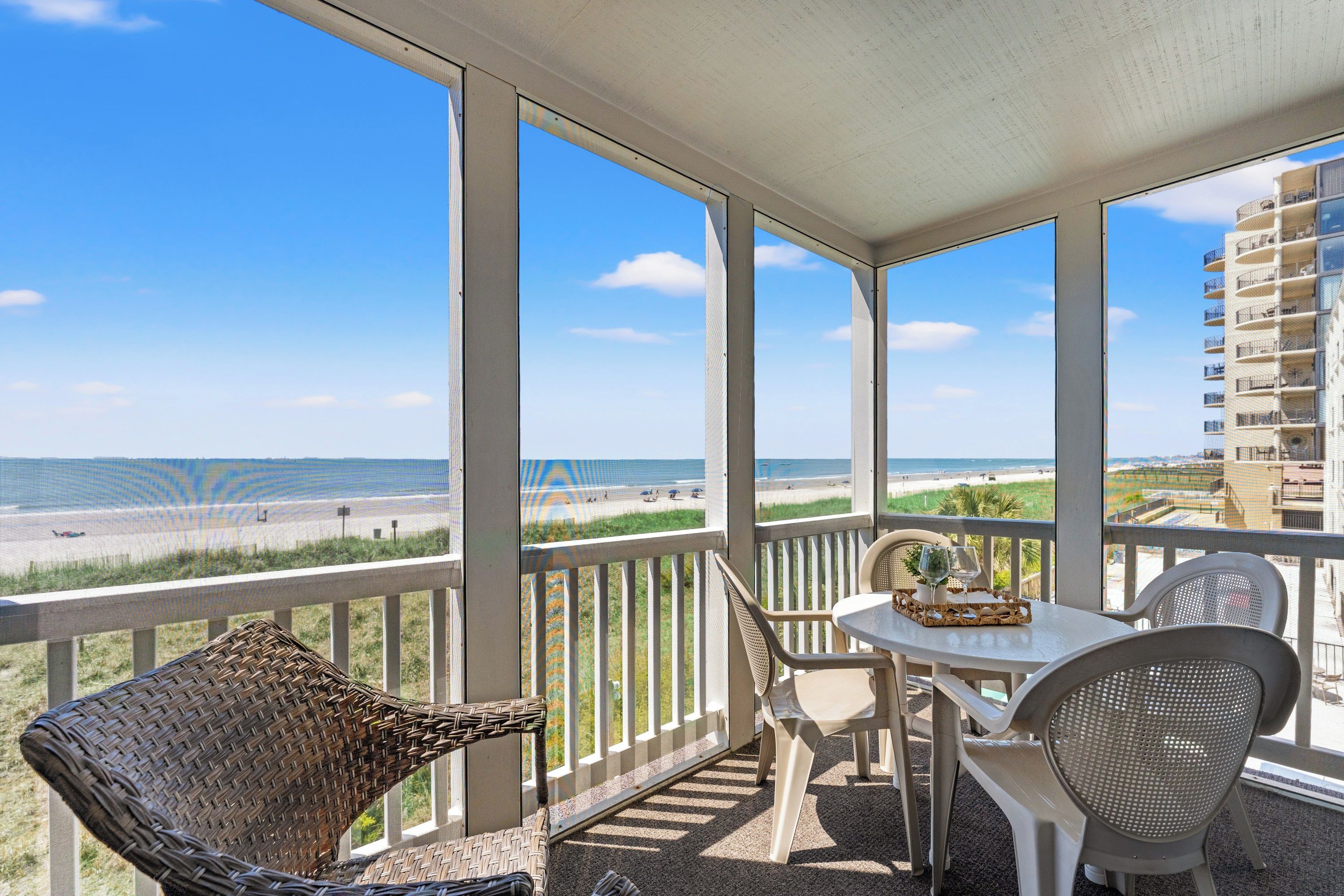 Een balkon met een tafel en stoelen, met uitzicht op een strand en een gebouw.
