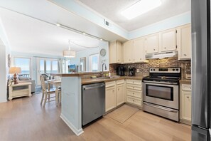 A modern kitchen with stainless steel appliances, light blue cabinetry, and a central island. - Dunescape 201-3BR/2.5BA Oceanfront condo in Crescent Beach (North Myrtle Beach)