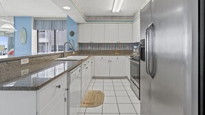 Cocina con gabinetes blancos, refrigerador de acero inoxidable y encimera de granito.