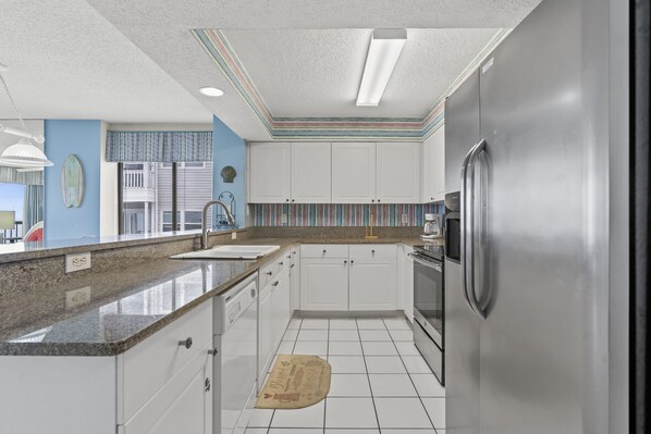 A kitchen with white cabinets, a stainless steel refrigerator, and a granite countertop.