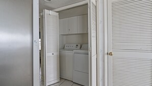 Un lavadero con lavadora y secadora, una puerta blanca y suelo de baldosas.