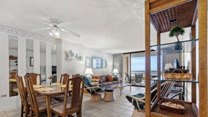 A spacious living room with a dining area, large windows, and a ceiling fan. - Ocean Creek North G5-2BR/2BA Oceanfront condo in Windy Hill (Myrtle Beach)