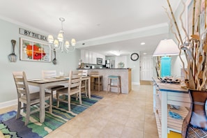 A spacious kitchen with white cabinets, a central island, and a dining area with wooden chairs and a rug.