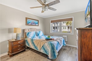 A bedroom with a bed, a nightstand, a ceiling fan, a window with a view, and a painting on the wall. - Palmwood Villas 104-2BR/2BA Oceanfront condo in Crescent Beach (North Myrtle Beach)