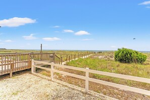 A coastal walkway with wooden railings, gravel path, and sparse vegetation.