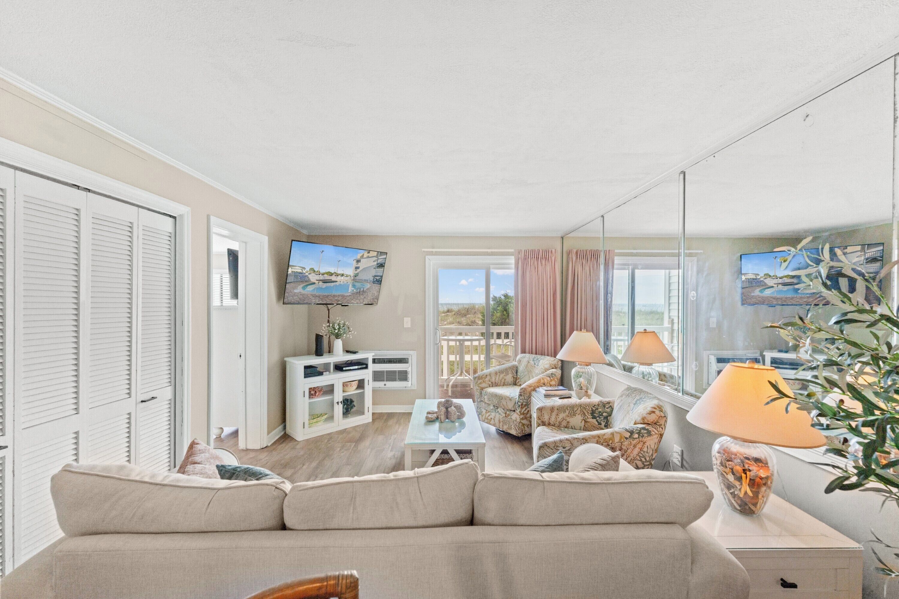 A living room with a sofa, armchairs, a coffee table, a TV, and a balcony with a view.