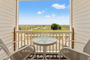 A balcony with a glass table and two chairs, overlooking a beach and a grassy area. - Sunvillas B1-2BR/2BA Oceanfront condo in Crescent Beach (North Myrtle Beach)
